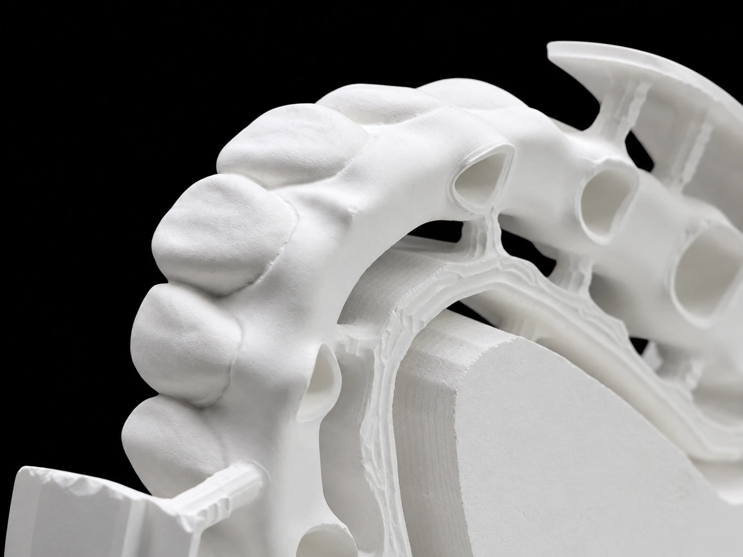 Close-up of a white zirconia bridge on a black background, showing tooth contours, openings and the disc support structure
